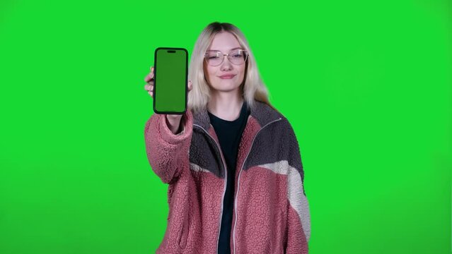 Woman showing mobile application modern smartphone mockup greenscreen in hand. Close-up blonde girl standing against the background of green chroma key
