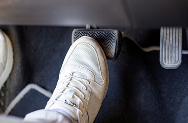 Pair of white sneakers on the floor in a car pressing brake against gas pedal, carefully driving...