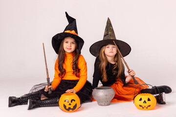 Two little girls in witch costumes having fun on Halloween and cook potion in a pot on white...