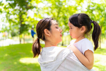 Happy Asian family enjoy and fun outdoor lifestyle travel together on summer holiday vacation. Mother carrying and playing with little daughter at public park in the city. Family relationship concept.
