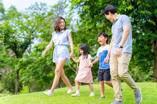 Happy Asian family spending time together travel on summer holiday vacation. Parent and little child enjoy and fun outdoor activity lifestyle walking and playing together at public park in the city. 
