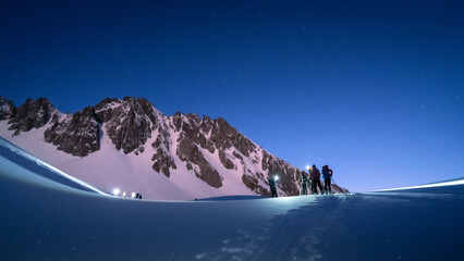 Skiers touring at night in the French alps in winter under the fullmoon light. fresh snow, stars, night sky