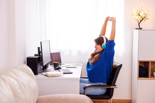Tired woman stretching out while sitting at her desk in home office - Powered by Adobe