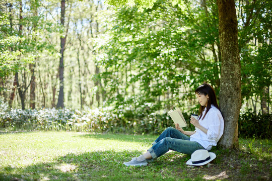 森の中でリラックスしながら読書をする30代日本人女性の初夏のイメージ
