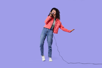 Beautiful young woman with microphone singing on purple background
