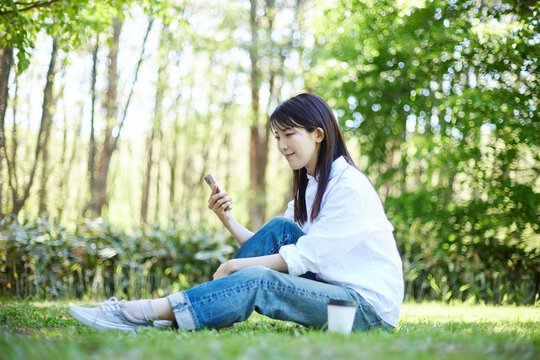 森の中でリラックスしながらスマートフォンを操作する30代日本人女性の初夏のイメージ