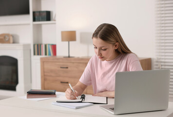 Online learning. Teenage girl writing in notepad near laptop at table