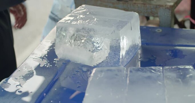 A large chunk of ice was cut with an axe and camera focus into axe.Close up hand cut ice.A man cut the ice into smaller cubes and crush them finely.	