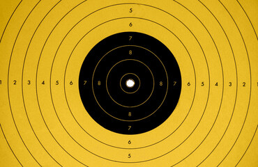 close up of a yellow and black target perfectly hit in the center by a bulletin a shooting gallery