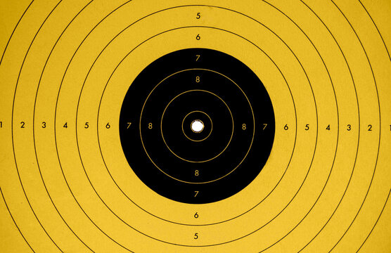 close up of a yellow and black target perfectly hit in the center by a bulletin a shooting gallery
