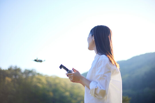 自然豊かな森の中でドローンの操縦をする日本人女性の夏のイメージ
