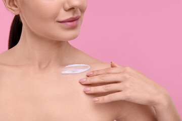 Obraz na płótnie Canvas Woman with smear of body cream on her collarbone against pink background, closeup