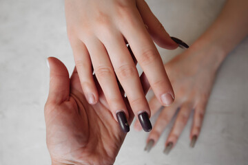 the manicurist holds the hand of a client with untidy broken nails, with an overgrown manicure to update