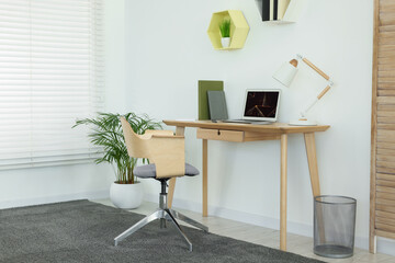 Cozy workspace with modern laptop on desk and comfortable chair at home