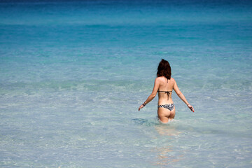 Slim woman in bikini going to swim in blue sea water. Beach vacation in hot weather