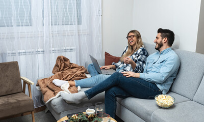 Young happy lovely couple planning budget together at home, writing notes to laptop computer, creating checklist for shopping or guest list for wedding invitations, counting chairs on ceremony