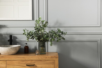 Stylish vessel sink and eucalyptus branches on bathroom vanity near grey wall, space for text. Interior design