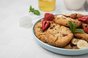 Cookies with freeze dried fruits, mint and nuts on white tiled table, closeup. Space for text