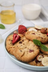 Cookies with freeze dried fruits, mint and nuts on white tiled table, closeup
