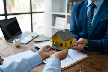 Real estate agent or sales manager is handing over a mockup house after offering terms and signing a home purchase contract and free home insurance, finance and after sales service concept.