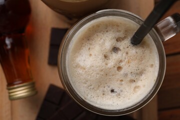 Glass of delicious coffee with chocolate syrup on wooden table, flat lay