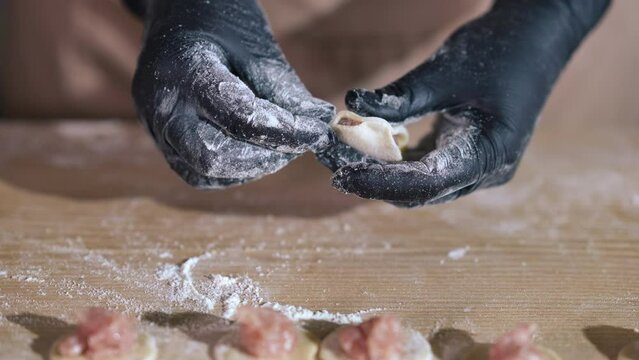 Closeup female hands in gloves forming meat dumplings indoors. Close-up unrecognizable Caucasian cook making raw food in cafe restaurant kitchen