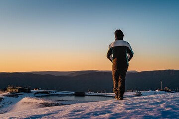 Rear of a man standing and enjoying winter landscape at sunrise, clear and purple sky background