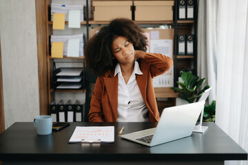 Overworked young African businesswoman office worker suffering from neck pain after had a long day at her office desk.