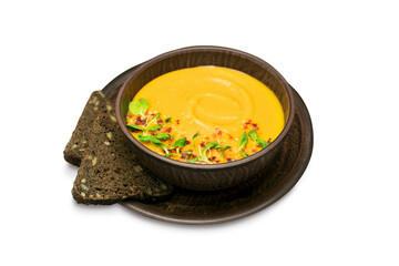 Vegetable cream pumpkin soup garnished with microgreens and chili flakes in a brown bowl with slices of black bread, isolated on a white background.