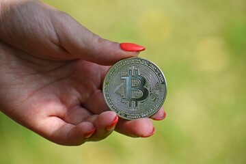 Woman's hand holding a silver bitcoin coin on a blurred background - concept of cryptocurrency