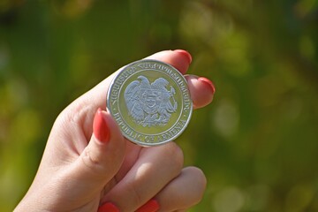Close up of a woman's hand holding a coin with the Coat of arms of Armenia on it, blurred background