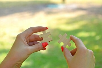 Woman's hands connecting jigsaw puzzle pieces on a natural background - concept of business strategy