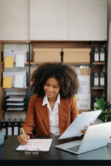 Confident beautiful African businesswoman typing laptop computer and digital tablet while holding coffee at office.