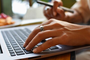Closeup shot of a young female working on her laptop and having a croissant in a cafe