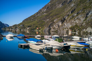 Lake Lugano surrounded by mountains and a small marina with moored boats on a sunny day