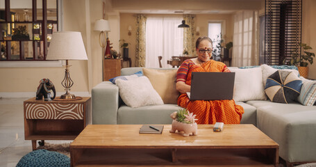 Elderly Indian Woman Using Laptop at Home: Immersed in Captivating Online Stories, Exploring New Ideas, NurturingLifelong Love for Learning. Celebrating the Beauty of Curiosity of Old Age. 