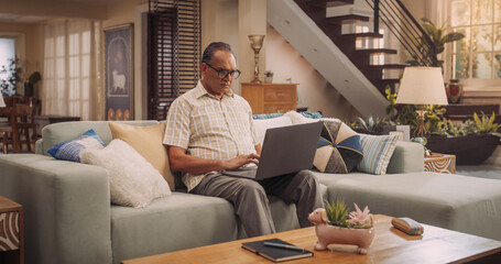 Elderly Indian Man Using Laptop at Home: Using Online Platforms to Explore His Interests, Delving...