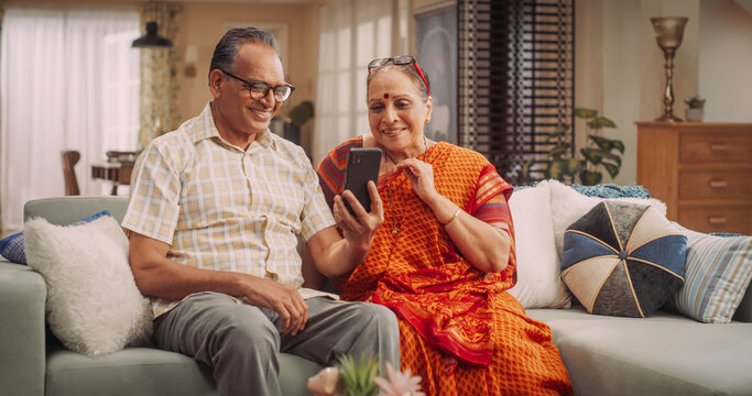 Elderly Couple Using Smartphone for Video Call at Home: Connecting with Loved Ones, Sharing Life's Moments, and Creating Lasting Memories. Embracing Technology to Stay Close. Medium Shot.
