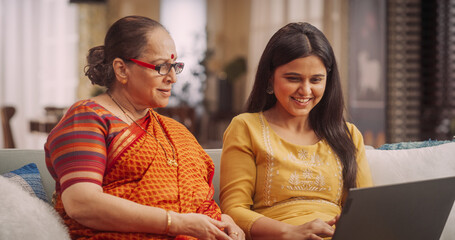 Portrait of an Elderly Woman and her Daughter Using Laptop Computer at Home: Smiling Girl Doing Online Shopping with her Mother, They are Watching Videos on Streaming Platforms and Social Media