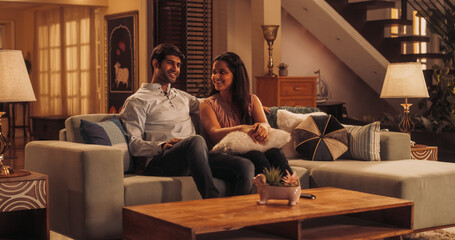 Movie Night: Young Couple Relaxing on the Couch, watching Exciting Movie on TV. Girlfriend and Boyfriend Embrace, Cuddle, Talk, Smile and watch Television Streaming Services in Cozy Home