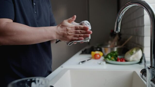 Close-up view of man wipes his hands after washing dishes in kitchen at home