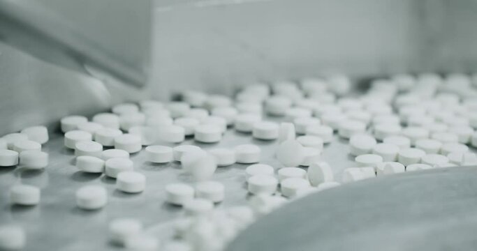White pills moving on metal automatic line in workshop of pharmaceutical factory. Process of production of pills, drugs. Factory equipment and machine conveyor. Industrial pharmaceutical concept.