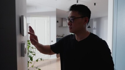 Handsome asian man turns on alarm system in house - Powered by Adobe