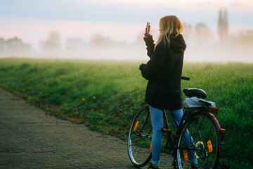 Young attractive caucasian woman making photo of beautiful view of sunset with fog while ride on...