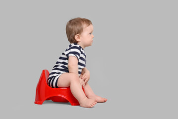 Little child sitting on baby potty against light grey background, space for text