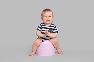 Little child sitting on baby potty against light grey background
