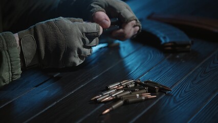 A soldier unloads the magazine of a Kalashnikov assault rifle, arranging cartridges on a wooden...