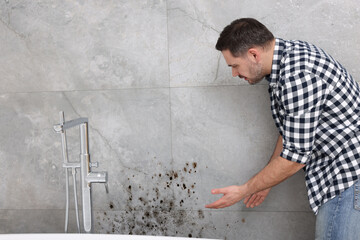 Man looking at affected with mold wall in bathroom