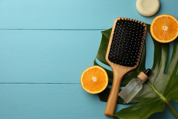 Hair brush, bottle of essential oil, dry shampoo and orange slices on light blue wooden table, flat lay