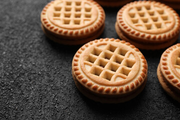 Tasty sandwich cookies with cream on black textured background, closeup. Space for text